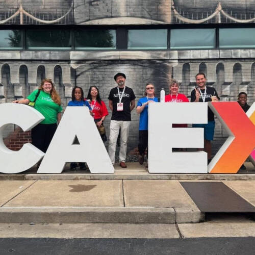 Teachers participating in the RCA Experience pose in front of a large sign.